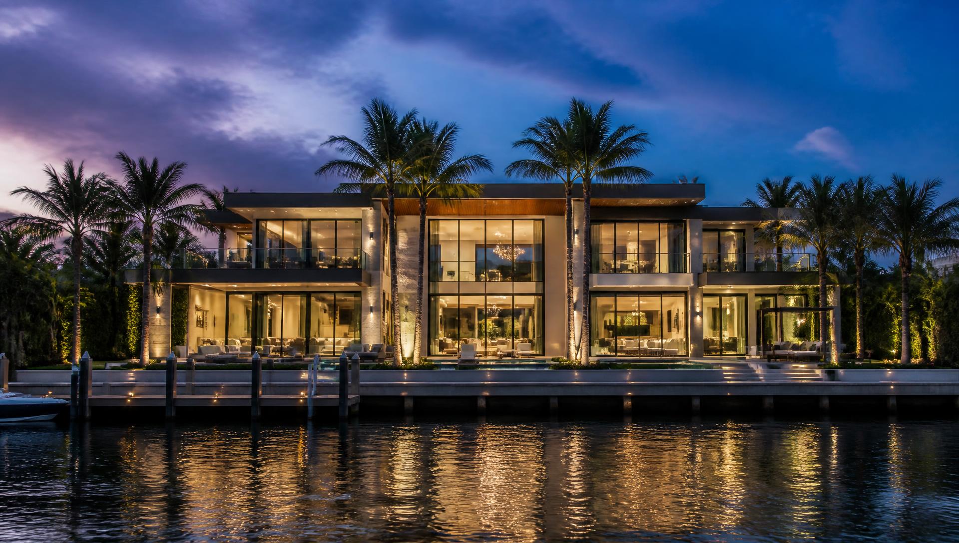 Waterfront estate at dusk with warm interior light reflecting on calm water